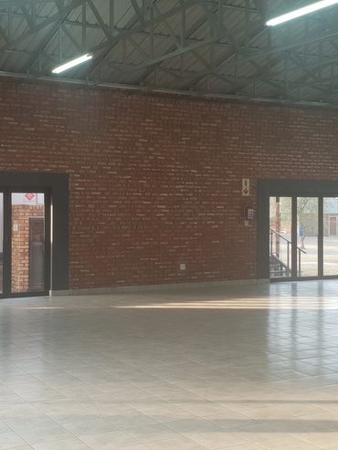 Empty spacious hall with brick walls and large glass doors letting in natural light.