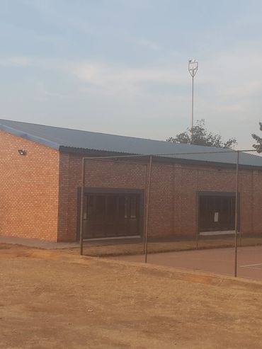 Brick building near a fenced basketball court with a two-story school building in the background.