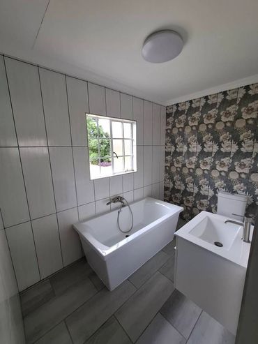 Modern bathroom with white bathtub, floral wallpaper, and grey tiled floor.