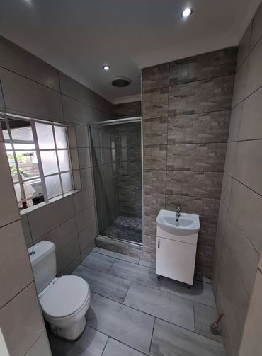 Modern bathroom with tiled walls, shower, toilet, and a compact white sink unit.