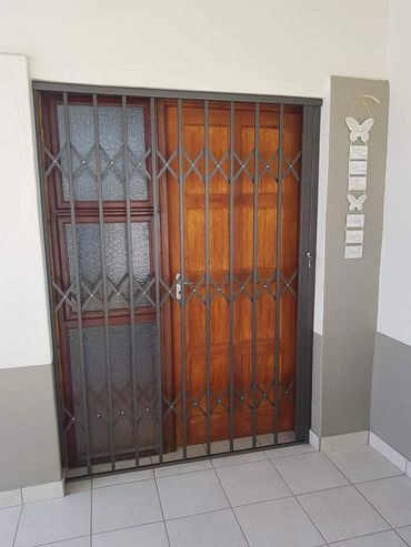 Wooden door behind a decorative metal security gate in a tiled entryway.