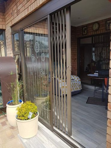 Sliding glass door with security gate and potted plants outside.