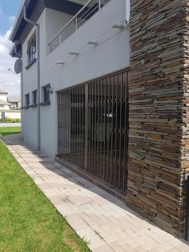 Modern house exterior with a stone pillar and metal security gate.