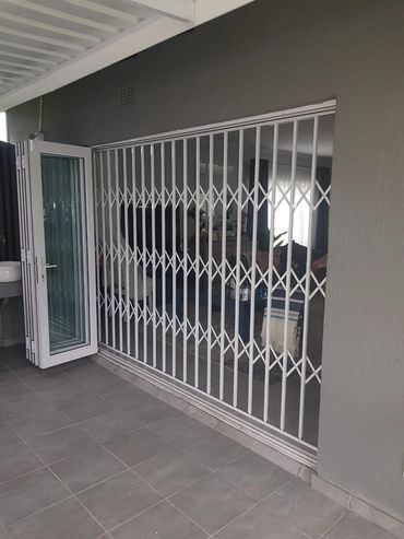 Foldable white security gate and glass door at a home entrance.