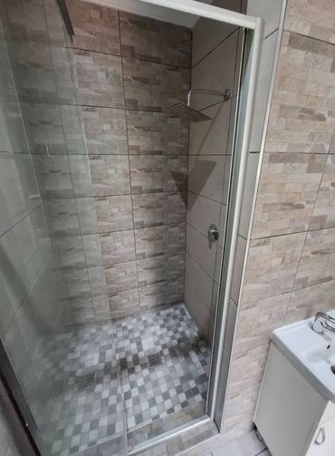 Modern shower area with glass door and tiled walls and floor.