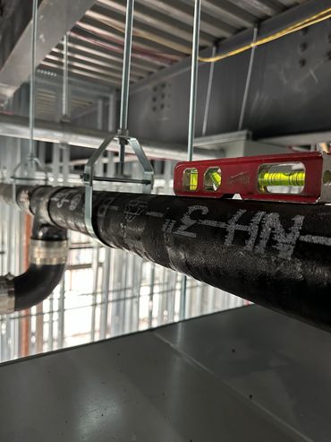 A level tool placed on a suspended black pipe in a construction setting.