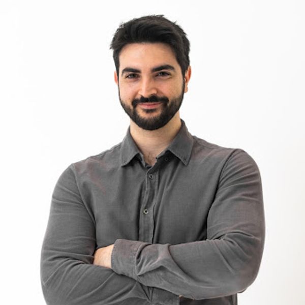 Confident man with beard in gray shirt smiling with arms crossed.