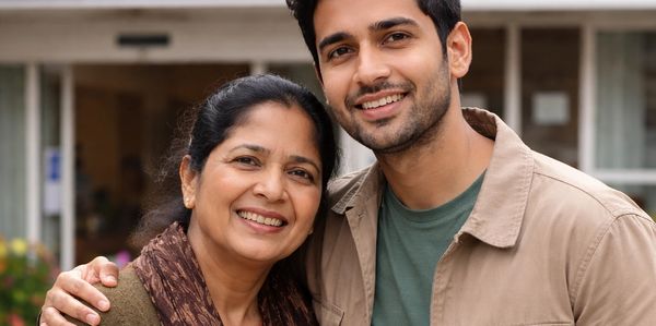 A smiling mother and son standing close together outdoors.