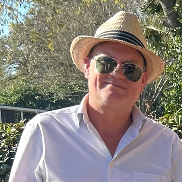 Man in a white shirt wearing a straw hat and sunglasses outdoors.