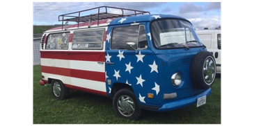 Vintage van painted with American flag design parked on grass.