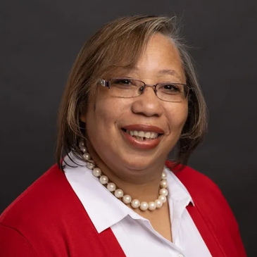 Smiling woman in glasses and red cardigan with pearl necklace.