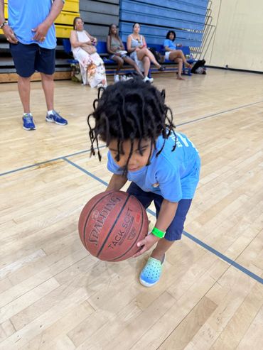 Young boy in blue shirt playing basketball indoors on court.