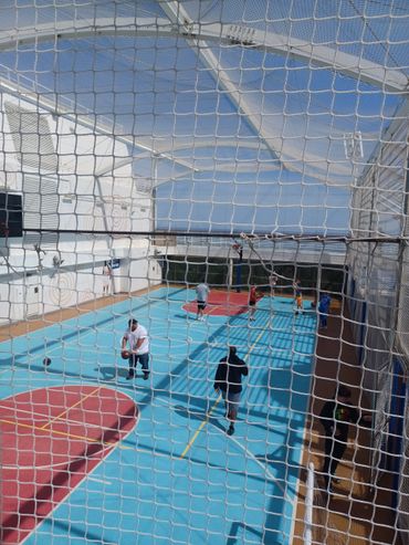 People playing basketball on a covered outdoor court with a bright blue floor.