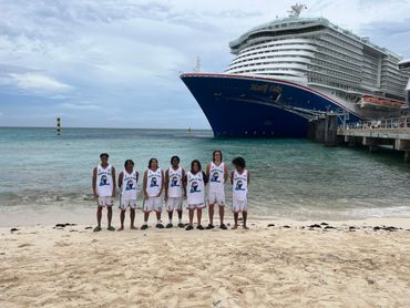 Youth basketball team posing on a beach with a large cruise ship docked nearby.