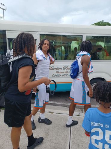 Young basketball players and a child standing near a bus, dressed in sportswear.