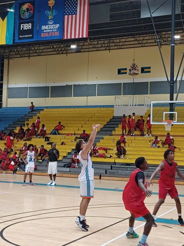Basketball players in action during a game in a gym with yellow bleachers.
