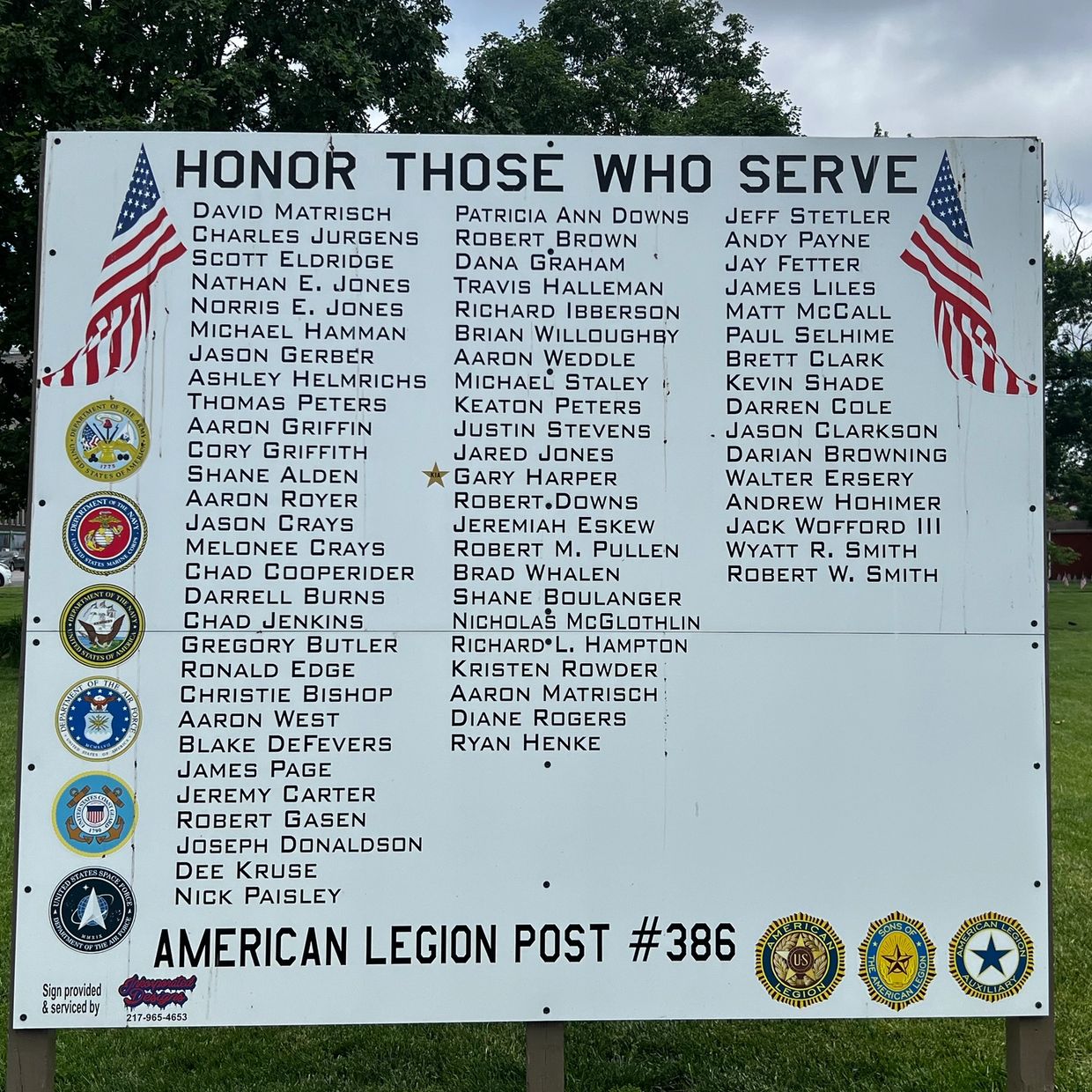 Memorial board honoring military service members with names and American flags.