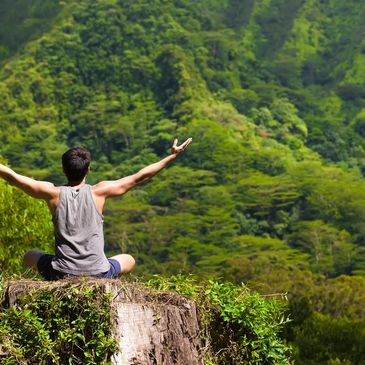 Young male student practices pranayama breath exercises in lush green mountain valley.