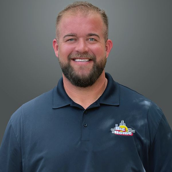 Smiling man with a beard wearing a navy blue polo shirt with a colorful logo.