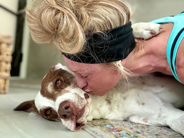 Woman kisses her dog affectionately while lying on the floor.