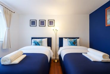 Two neatly made beds with blue bedding and white towels in a bright room.