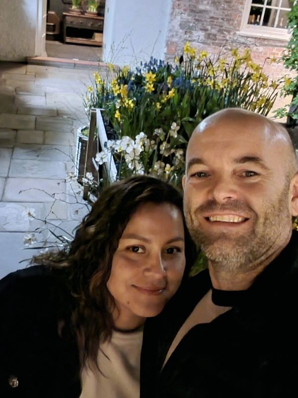 A smiling couple posing for a selfie near a flower bed at night.