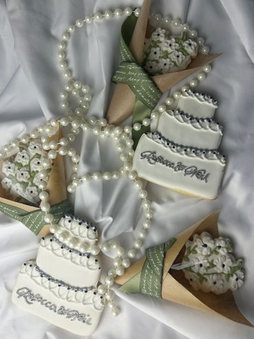 White wedding cake royal icing cookies with pearl detail alongside bouquet cone cookies, personalize