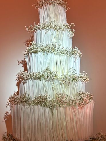 Multi-tiered white wedding cake with vertical rice paper ruffle panels and baby's breath floral acce