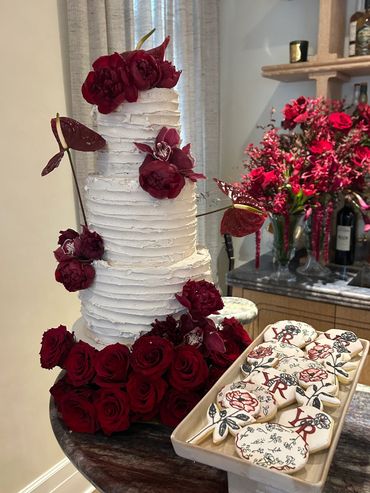 Multi-tiered white buttercream wedding cake with horizontal textured finish, decorated with deep red
