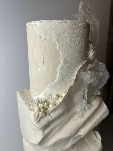 Two-tiered white structured-fondant wedding cake with a textured geological fault-line design, sugar