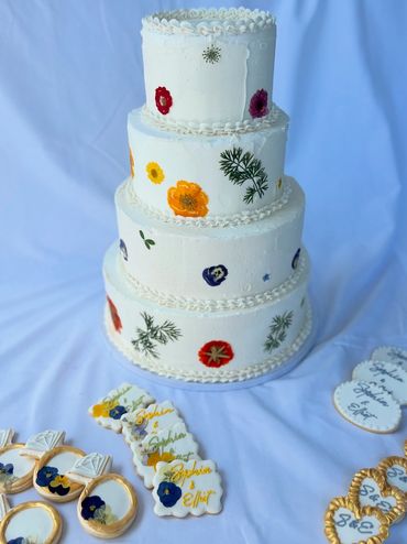 Three-tiered white fondant wedding cake decorated with colorful pressed flowers in red, orange, yell