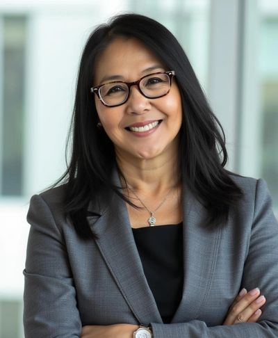 Confident woman in glasses and gray blazer smiling with arms crossed.