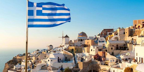Greek flag waving over Santorini's iconic white buildings at sunset.