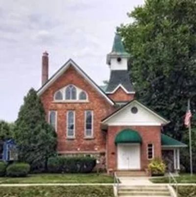 A charming brick church with a steeple and green canopy entrance.