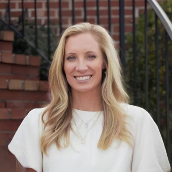 A smiling woman with long blonde hair in a white top.