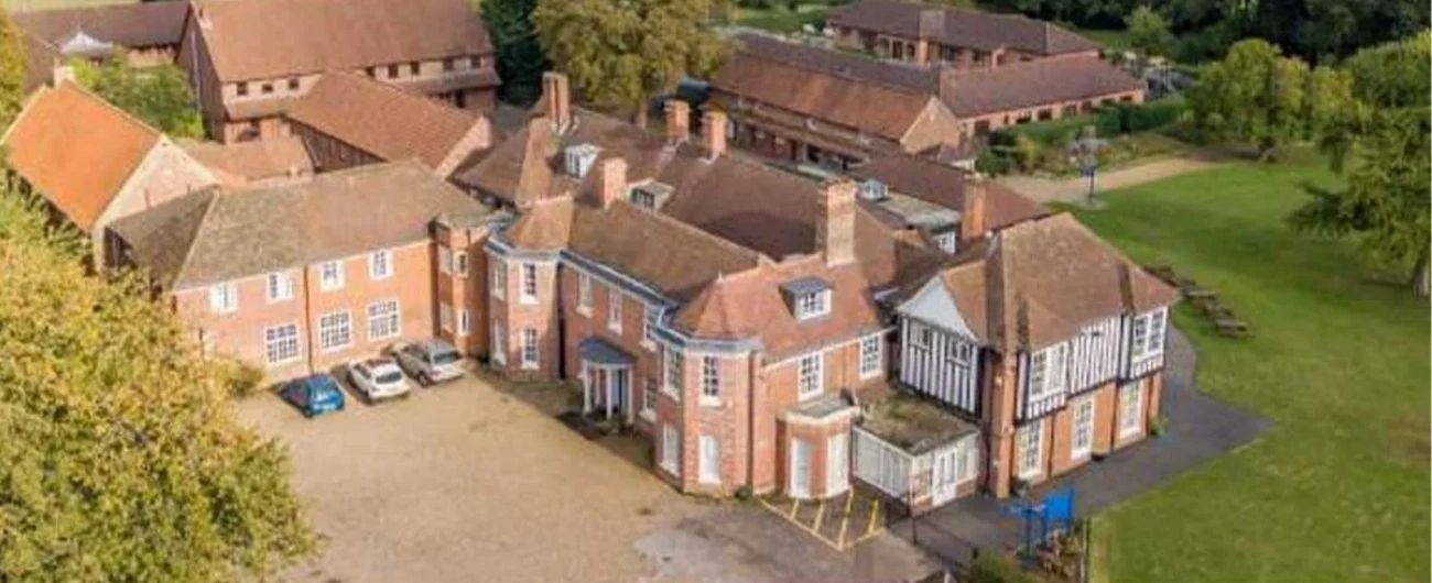 A large historic building complex surrounded by greenery and parking area.