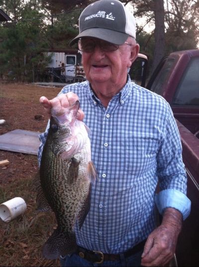 Elderly man proudly holds a large fish he caught outdoors.