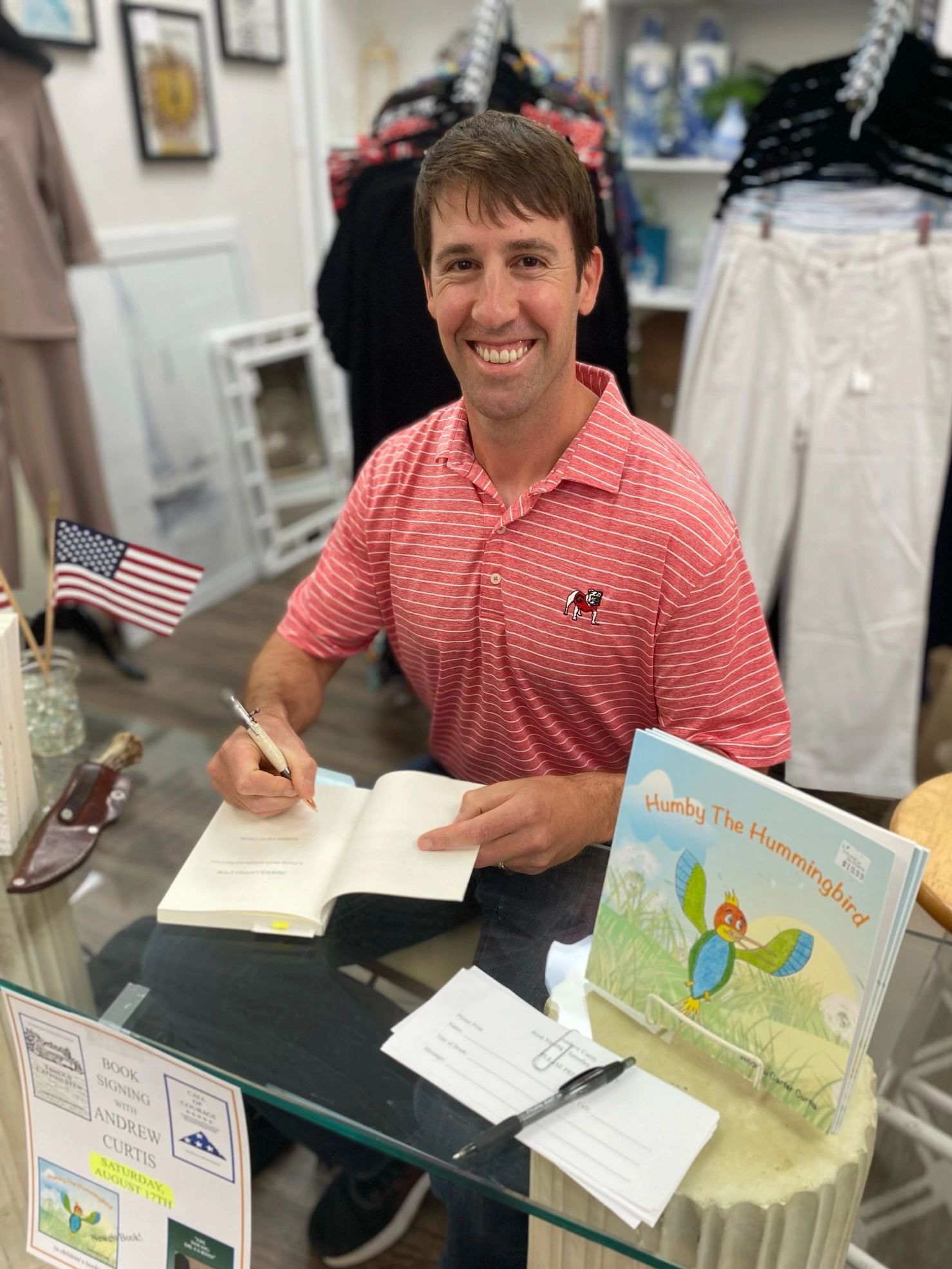 A smiling man signs a book at a signing event.
