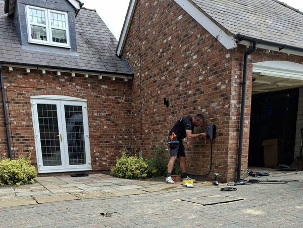 Technician installing an outdoor electrical device on a brick house wall.