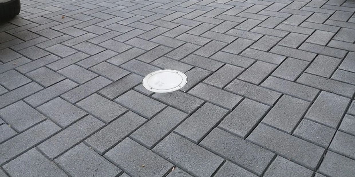 Gray brick pavement with a round white cover.