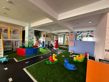 Colorful indoor playroom with toy rockers and mini playhouses.