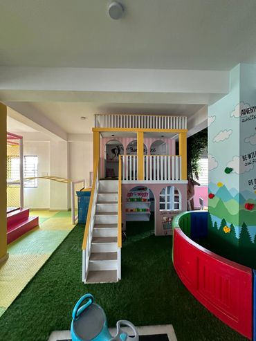 Indoor children's play area with a small house, slide, and climbing wall.