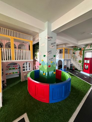Colorful indoor kids' play area with climbing wall and miniature houses.