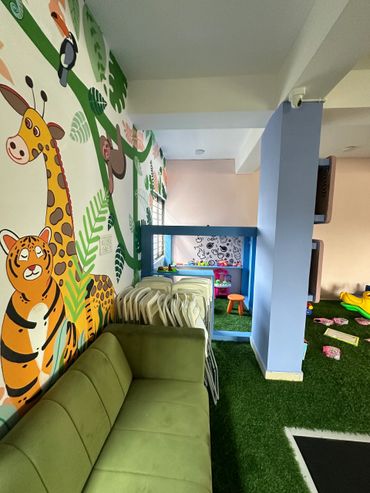 Colorful indoor playroom with animal wall murals and green sofa seating.