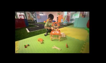 A young boy playing with a wooden toy toolset on a colorful foam mat.