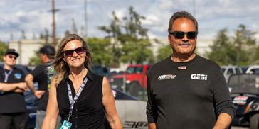 A man and woman wearing sunglasses walk outdoors smiling.