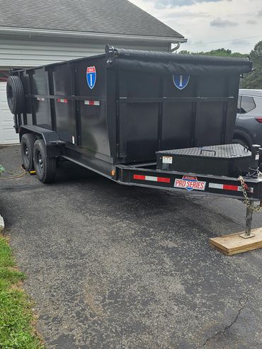 Black utility trailer with dual axles parked outside.