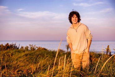 smiling young man in sweater at beach against purple and pink sunset