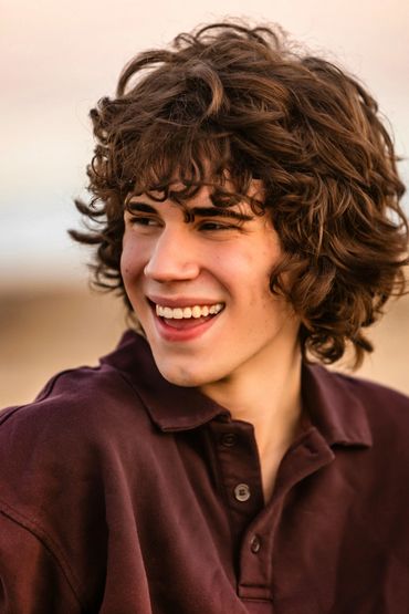 smiling young man with long curly brown hair