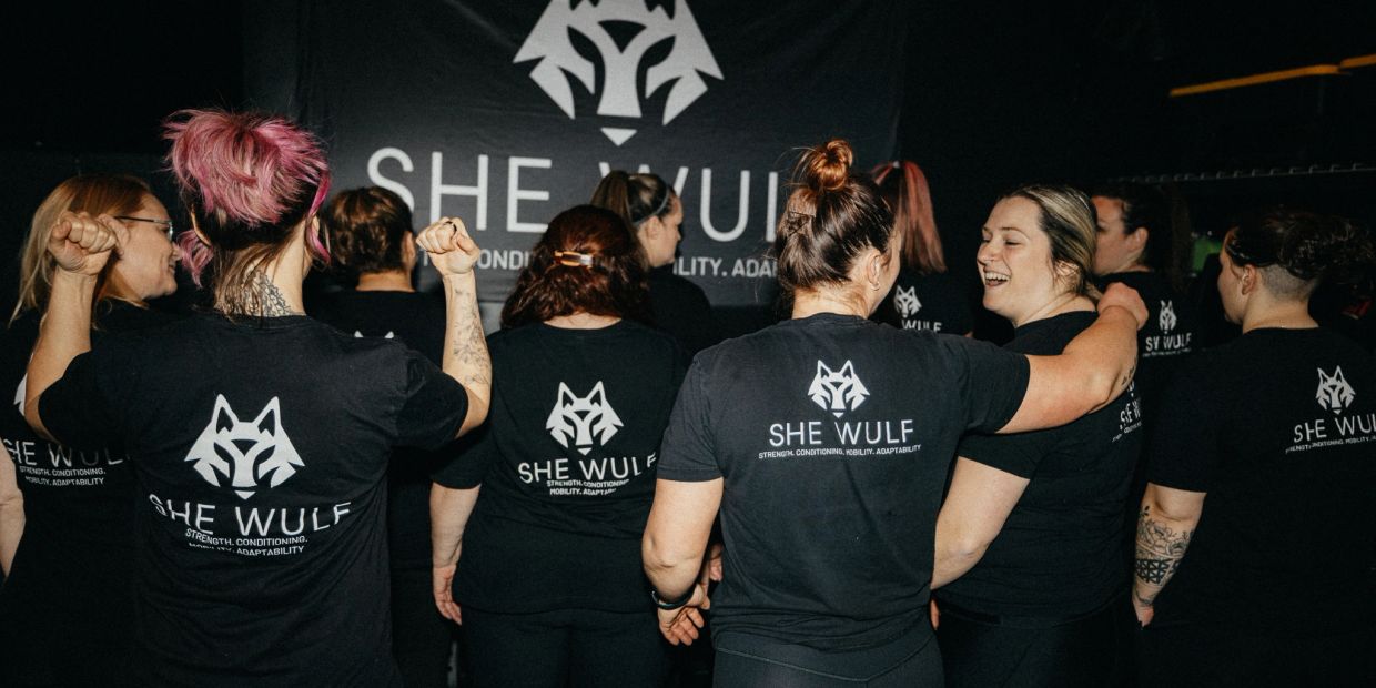 Group of women in She Wulf shirts at a gym or fitness center.